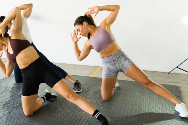 Parlak fitness sınıfında üç kişi yan atlama egzersizi yapıyor.