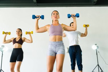 Parlak bir spor salonunda ağırlık kaldırmaya odaklanmış üç kişi.