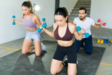 Üç arkadaş beden eğitimi dersinde senkronize halter egzersizi yapıyor.