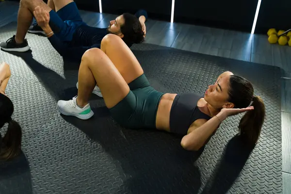 Kapalı alanda mekik egzersizine katılan katılımcılar, çekirdek kuvvete odaklanıyorlar.