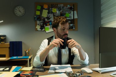 Özel dedektif gece geç saatlerde dağınık bir masada ipuçlarını incelerken kahveyi yudumluyor.