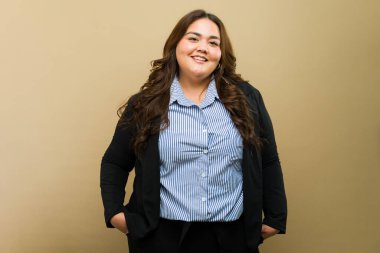 Tarafsız bir arkaplanda, bir portrede gülümseyen, iri yarı bir iş kadını pozu veriyor.