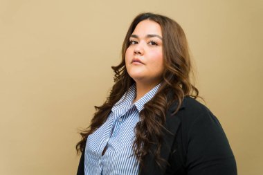 Tarafsız bir zemine karşı profesyonel giyimli kendinden emin, iri yarı bir iş kadınının portresi.