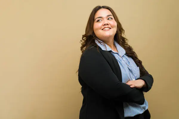 Confident plus-size woman in professional attire posing with a smile against a beige background
