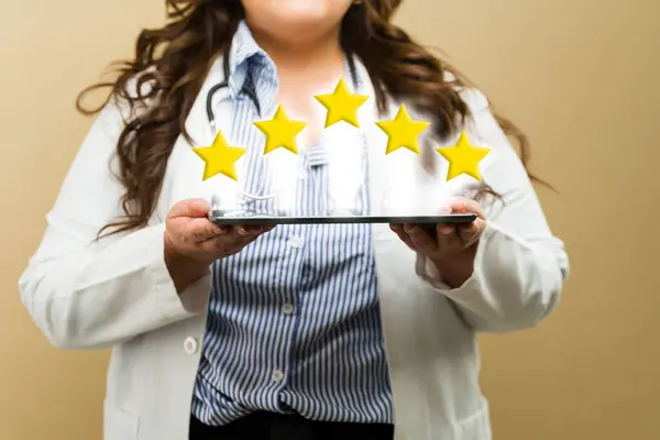 タブレットで5つ星のレビューを披露するプラスサイズの女性医師 優れたサービスを促進 近くで見た ストック画像