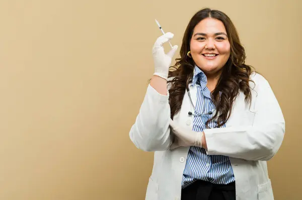自信に満ちたプラスサイズの女性医師が笑顔で いくつかのコピースペースでスタジオに注射器を保持し ワクチンの準備ができています ロイヤリティフリーのストック画像