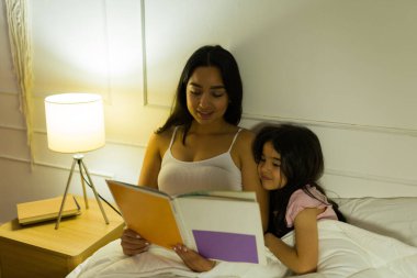 Huzurlu Latin anne, geceleri sıcak yatak odalarının yumuşak parıltısında genç kızına kitap okuyor.