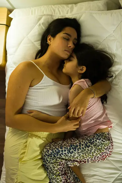 stock image Peaceful scene capturing a tender moment between a hispanic mother and her daughter, snuggled up in bed at home during the evening