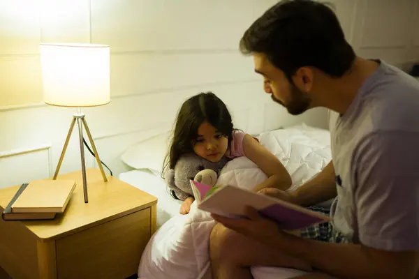 カーリングの父親は 寝る前にラップライトで娘に読んで 夜は居心地の良い寝室で暖かく親密な雰囲気を作ります ストック画像
