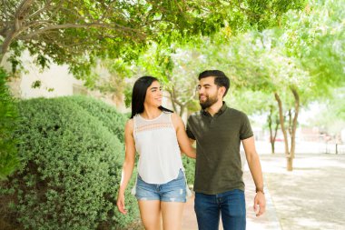 Genç latin çift dışarıda birlikte gülüyor ve yürüyorlar, güneşli bir günde parkta romantik bir buluşmanın keyfini çıkarıyorlar.