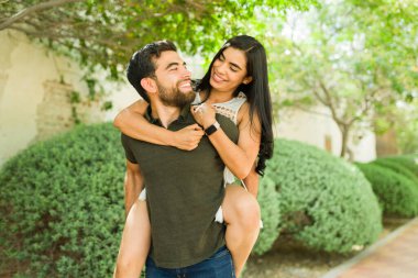 Mutlu genç çift dışarıda güneşli bir günde gülüyor ve kucaklaşıyorlar. Romantik ilişkilerinin sevgi ve bağlarını gösteriyorlar.