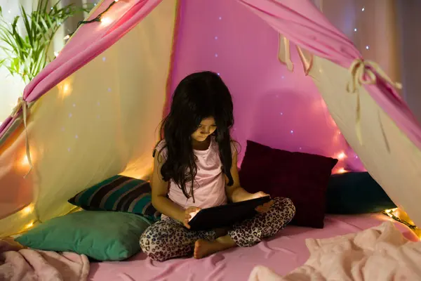 라틴어 히스패닉 소녀는 따뜻한 조명에 Makeshift 내부의 디지털 태블릿에 만족스럽게 스톡 이미지