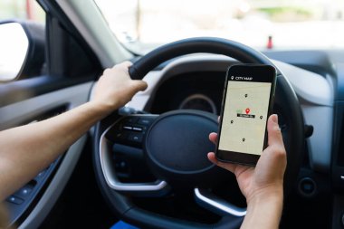 Kadın sürücü, arabasını sürerken rotayı bulmak için navigasyon uygulamalı bir cep telefonu kullanıyor ve modern seyahat teknolojisini gösteriyor.