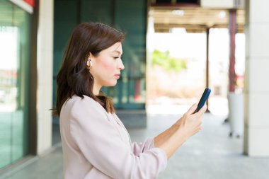 Şehir ortamında işe gidip gelirken akıllı telefon ve kulaklık kullanan bir iş kadınının profil görüntüsü modern iş hayatı entegrasyonunu gösteriyor