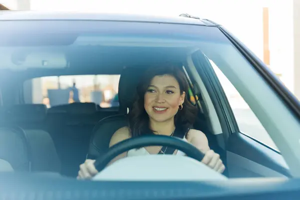 Smiling woman confidently driving her car, hands on the wheel, with a focus on safety and comfort in urban settings