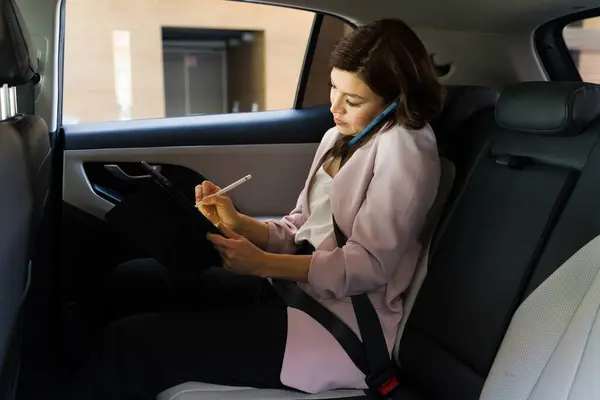 Professional Businesswoman Taking Notes Tablet While Riding Car Epitomizing Productivity รูปภาพสต็อก
