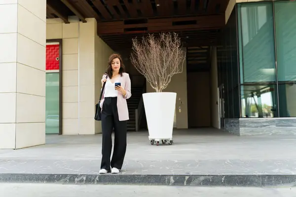 Professional Woman Stands Modern Office Focused Her Phone Hailing Ride รูปภาพสต็อก