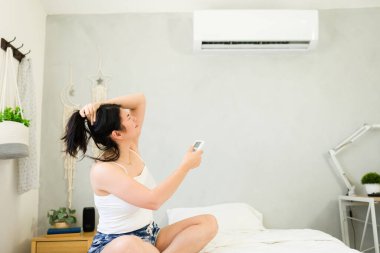 Woman relaxing on her bed, enjoying the refreshing breeze from a mini split ac unit on a hot summer day