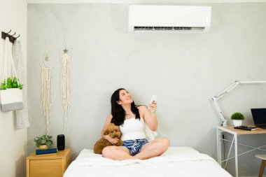 Smiling woman with a remote control enjoys the cooling breeze from a mini split air conditioning unit on a hot summer day