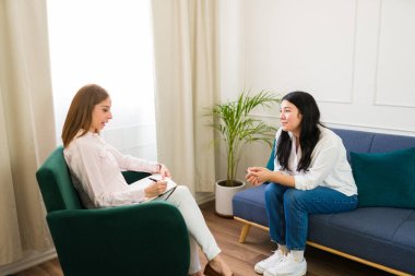 Focused woman psychologist attentively listens to a patient during a mental health therapy session in a calm, bright office environment