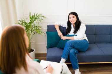 Woman talking while her psychologist attentively listens to herduring a therapy session, promoting mental health in a comfortable office
