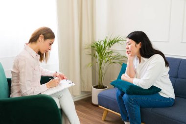 Professional female psychologist attentively taking notes as her female patient discusses mental health concerns during a therapeutic session