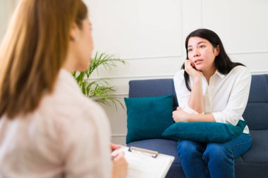 Woman talking during a therapy session while a focused psychologist attentively listens in a comforting therapy room