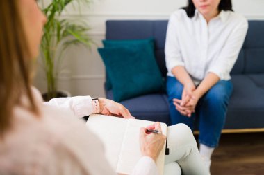 Professional female psychologist taking notes during a therapy session with patient focusing on mental health
