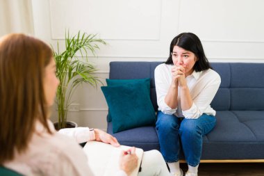 Focused female therapist attentively listens to a young woman during a therapy session, fostering a supportive mental health environment