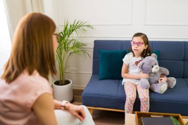 Child psychologist engaged in a therapy session with a young girl cuddling a teddy bear, creating a supportive environment for children