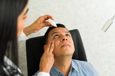 Standart göz muayenesi sırasında hastanın gözüne göz damlası damlatan bir klinikte konsantre göz doktoru.