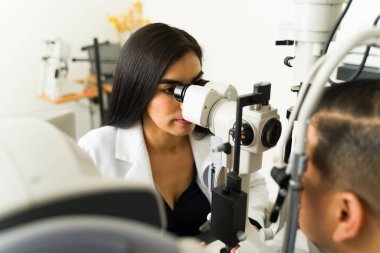 Klinik ortamda erkek bir hastanın göz sağlığını değerlendirmek için kesik lamba kullanan uzman bir göz doktoru.