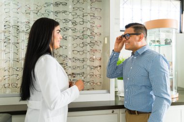 Dost canlısı göz doktoru, gülümseyen bir erkek hastaya modern bir gözlükçünün ofisinde yeni gözlük seçmesinde yardımcı oluyor.