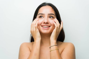 Çıplak omuzlu neşeli İspanyol kadın cilt bakımı yapıyor, parlak derisini parlak bir stüdyo ortamında sergiliyor.