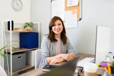 Neşeli kadın girişimci masasında çalışıyor. Parlak bir ofis, kendine güveni ve mesleki memnuniyeti var.