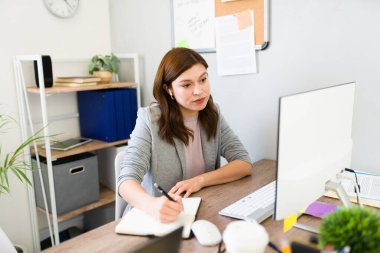 Profesyonel kadın, bilgisayar ve not defteriyle birlikte iyi organize edilmiş bir ofis masasında yeni başlattığı proje üzerinde çalışıyor.