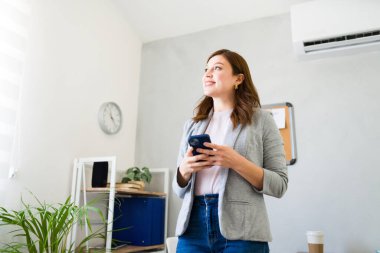Modern bir ofis ortamında gülümseyen akıllı telefonlu iyimser bayan girişimci, başarı ve güveni yansıtıyor