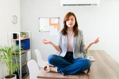Serene kadın girişimci, daha iyi odaklanmak ve stres atmak için yoğun bir başlangıç ofisinde masasında meditasyon yapıyor.