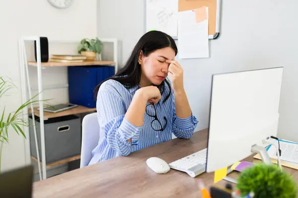 stock image Professional woman in a business office setting looks exhausted and stressed, showing eyestrain in front of her computer