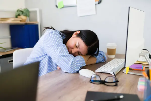 stock image Young woman in a striped shirt takes a power nap at her cluttered workspace, signifying exhaustion during a busy workday