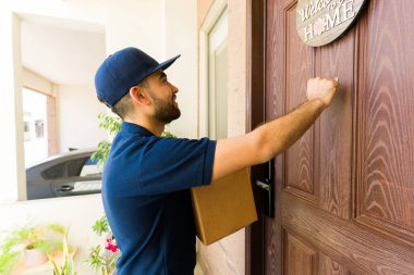 Paket taşıyan mutlu teslimatçı bir paket teslim etmek için evin ön kapısını çalıyor.