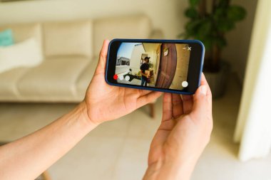 Bir kadının akıllı telefon uygulaması kullanarak teslimatçıyı paketini bırakırken izlemesi.