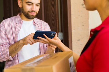 Teslimatçı kadın paketini tutuyor ve ön kapıda dijital imza için akıllı telefonu müşteriye gösteriyor.