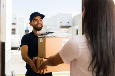 Karton kutular taşıyan mutlu teslimatçı ve kapısının önünde duran kadın müşteriye bir paket teslim ediyor.