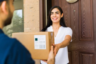 Mutlu kadın evinin girişindeki teslimatçıdan bir paket alıyor.