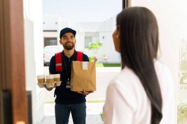 Evinin ön kapısındaki müşteriye paket yiyecek ve kahve getiren mutlu teslimatçı.