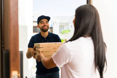 Neşeli pizzacı çocuk elinde pizza kutularıyla bir kadına yemek siparişi veriyor.