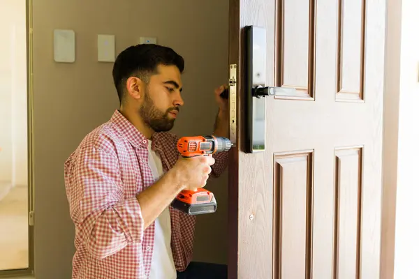 stock image Experienced handyman is carefully installing a smart lock on a front door, using a screwdriver to ensure a strong and secure attachment