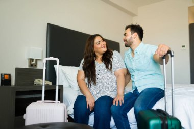 Genç çift, bagajlarıyla birlikte otel odasındaki yataklarında otururken tatillerinin tadını çıkarıyorlar.