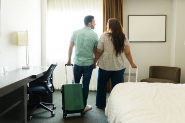 Genç çift otel odalarında el ele tutuşuyorlar ve bavullarıyla vardıkları yere vardıktan sonra tatile başlamaya hazırlar.